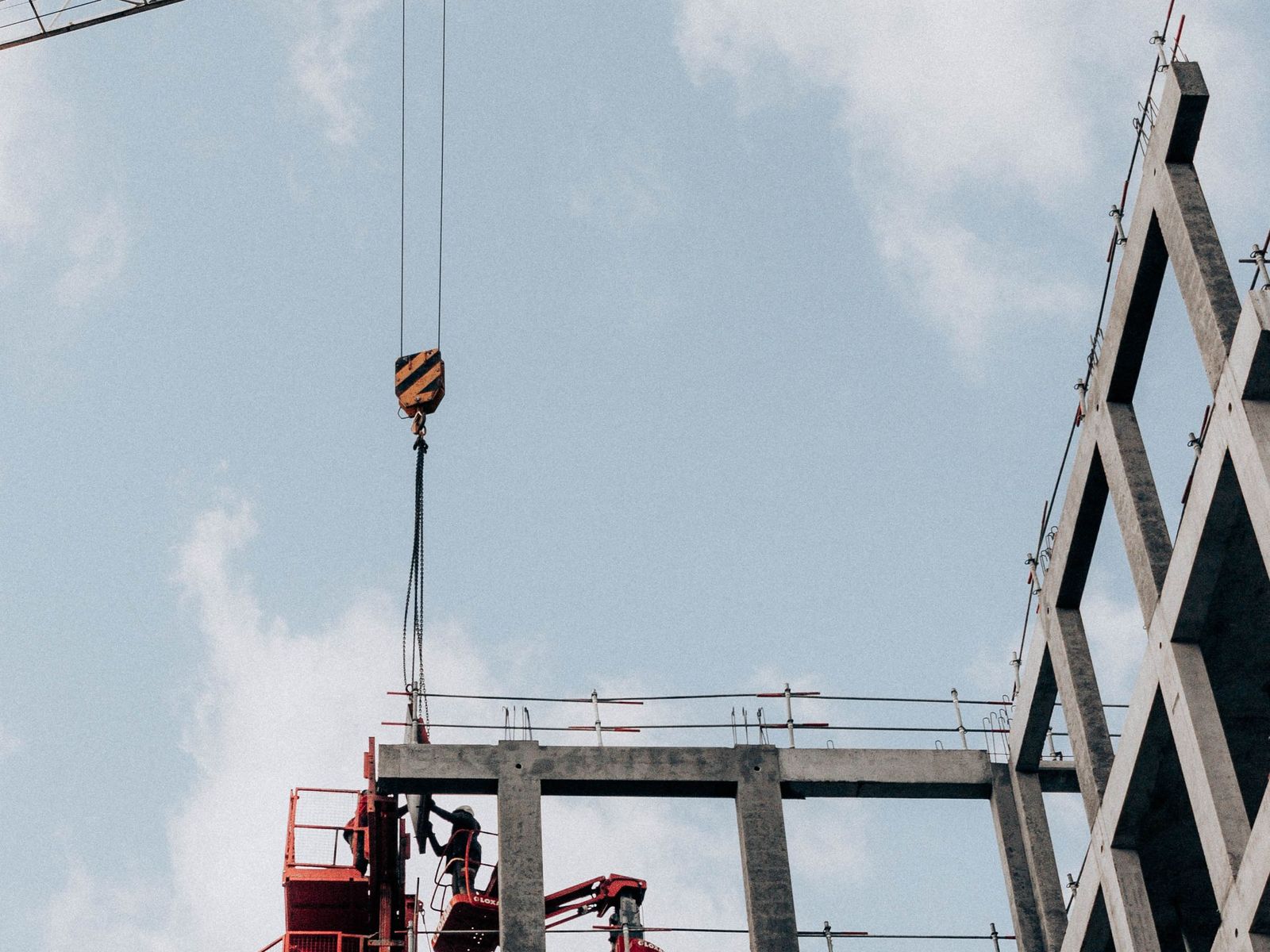 Betonnen casco in aanbouw met de giek en hijshaak van een torenkraan tegen een lichtbewolkte lucht
