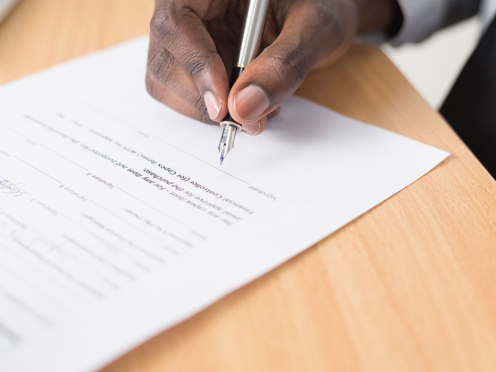 Hand met een zilveren vulpen die een contract ondertekent op een licht houten bureau